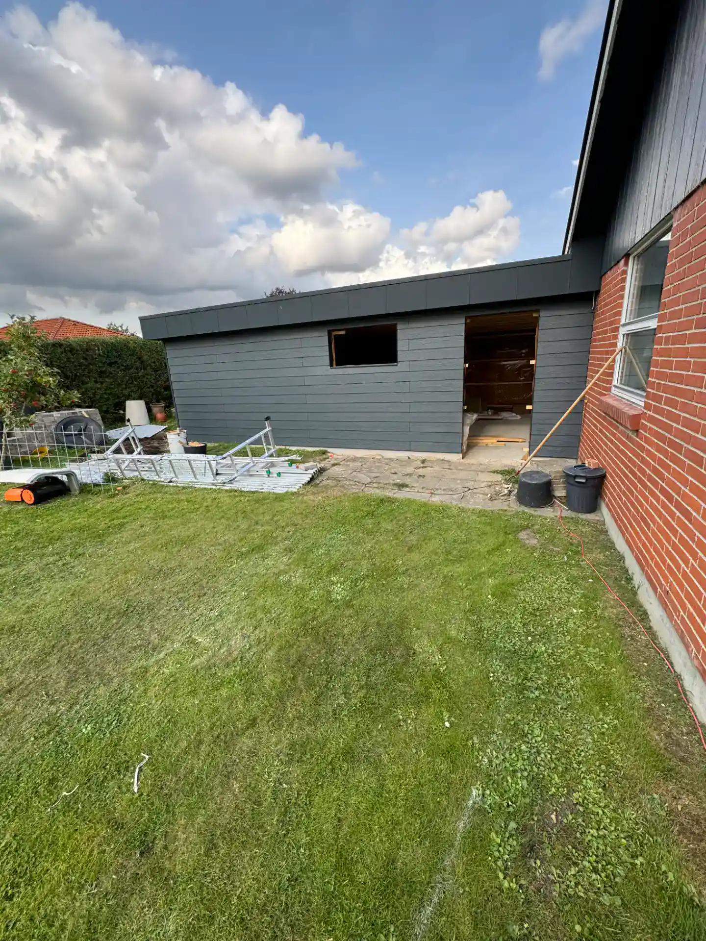 Nybyggeri af udhus med grå facade og trædør ved bolig.