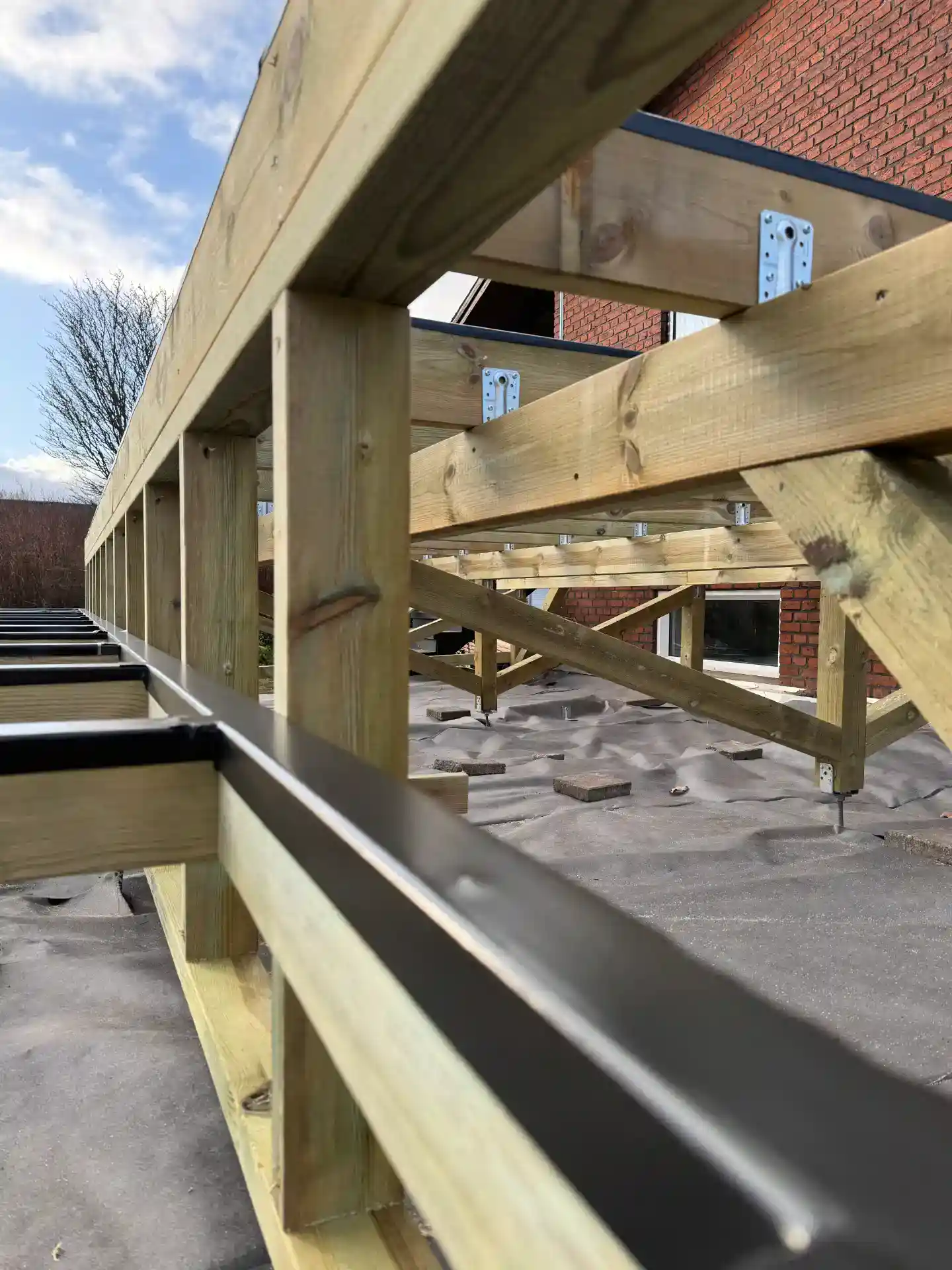 Træramme til terrasse under konstruktion med synlige træbjælker og metalbeslag.
