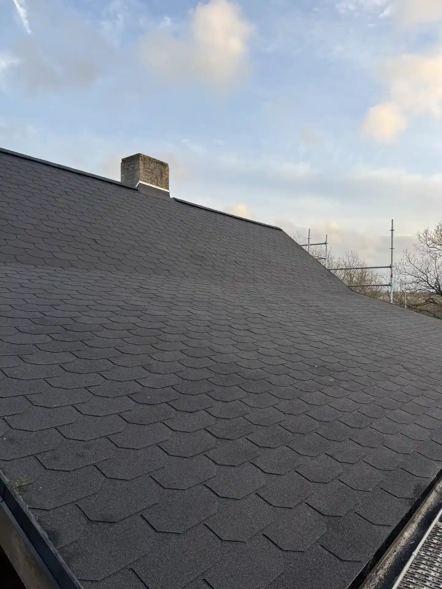 Sort tagdækning med tagsten på bolig med skorsten og himmel i baggrunden.